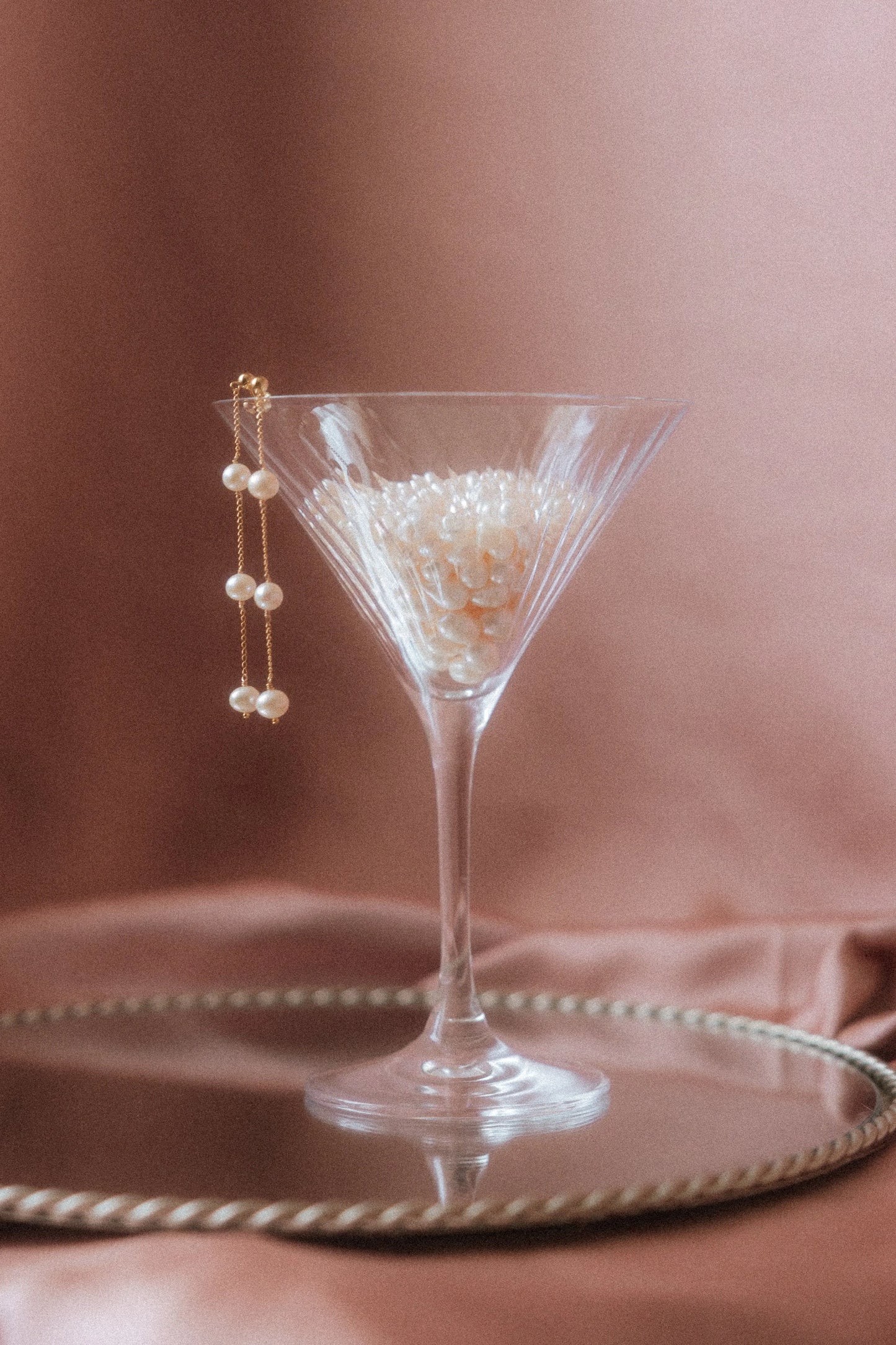 Boucles d'oreilles de mariage élégantes posées sur un verre rempli de perles d'eau douce