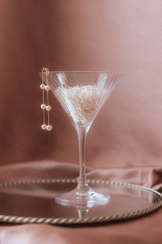 Boucles d'oreilles de mariage élégantes posées sur un verre rempli de perles d'eau douce